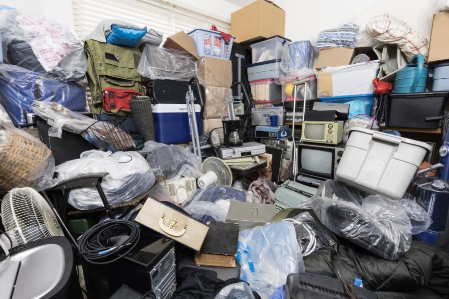 Cluttered room filled with piled boxes, bags, appliances, and miscellaneous household items